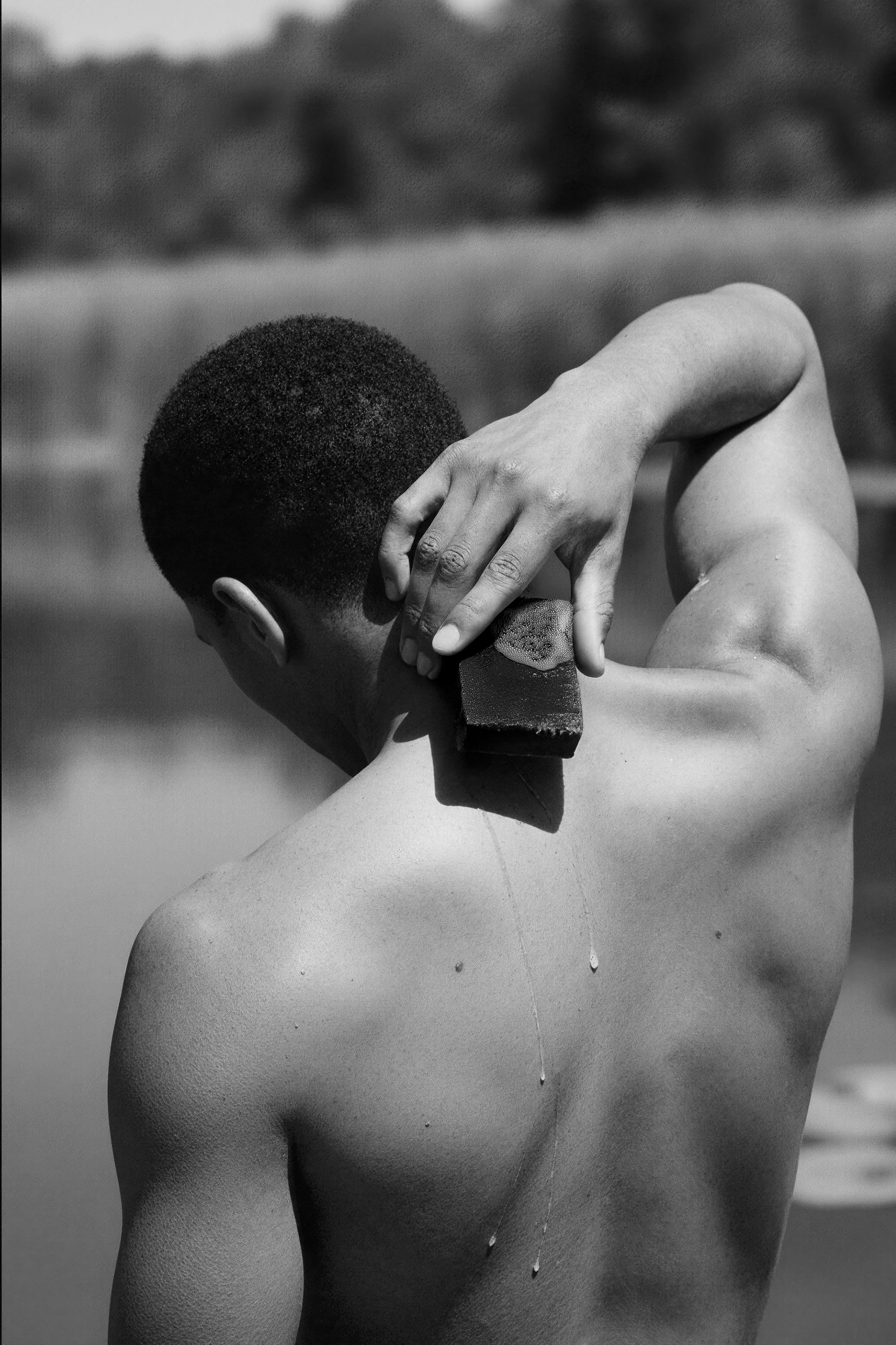 Man scrubbing their back with a OUMA soap bar, B&W image